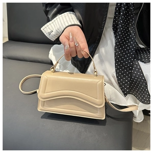 Close-up of beige crossbody bag featuring wavy flap design and gold hardware detail