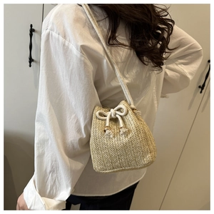 Detail of woven straw bucket bag with white drawstring closure and gold bead accents