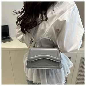 Gray crossbody small square bag with wavy flap detail shown on a female model