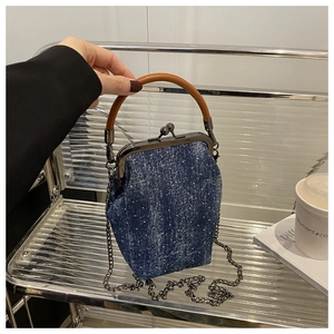 Détail d'un sac bandoulière en denim avec fermoir métallique et poignée en cuir sur étagère