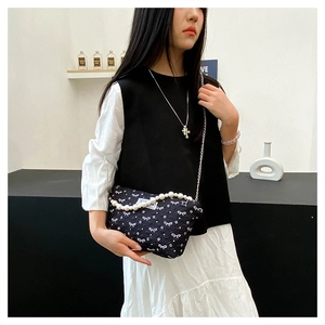 Détail d'un sac bandoulière noir avec motifs de nœuds blancs et anse en perles