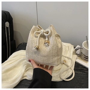 Detail of beige woven straw bucket bag with cotton drawstring and gold metal buckle