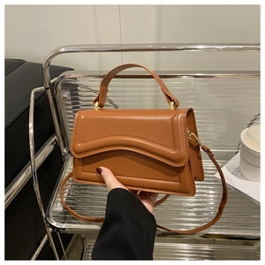 Detail of caramel brown leather handbag with unique wave-shaped flap and fine stitching