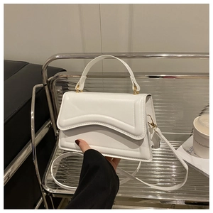 Close-up of white leather handbag featuring wavy stitching and elegant gold hardware