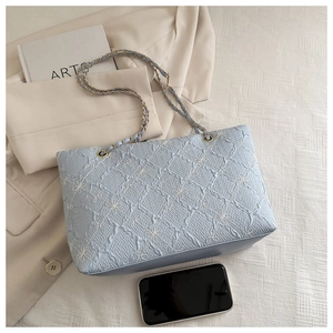Detail of light blue quilted tote with floral embroidery and gold chain strap