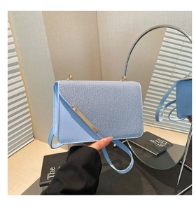 Detail of light blue crossbody bag featuring mixed textures and gold metal trim accent