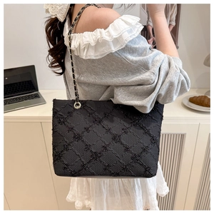 Detailed view of black quilted chain tote bag with sequins worn on person's shoulder