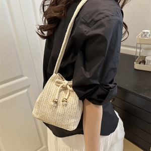 Woven straw bucket bag with drawstring closure and gold ball details for beach vacations