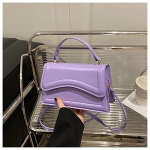 Detail of purple leather handbag featuring unique wave-pattern flap and metal handle