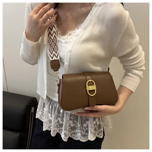 Detail of a brown leather shoulder bag with a gold horseshoe buckle and patterned strap