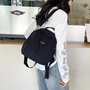 Large black nylon backpack for women, stylish minimalist travel bag shown in cafe setting