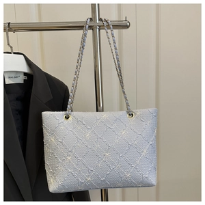 Close-up of light blue quilted tote bag with floral embroidery and gold chain strap