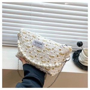 Détail du sac à cosmétiques blanc texturé avec papillons dorés et poignée de perles
