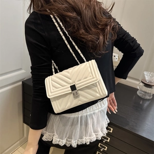 Chic beige quilted chain shoulder bag with metal lock worn by a model in a stylish outfit