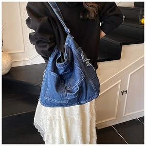 Detail of large blue denim tote bag with multiple utility pockets and frayed edges