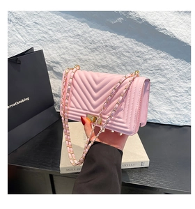 Sac à bandoulière rose clair matelassé avec chaîne dorée tenu dans un décor épuré