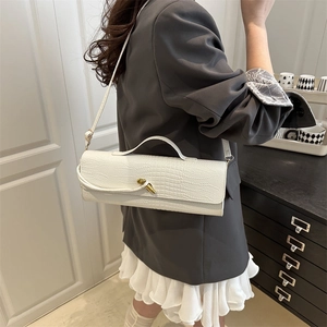 White crocodile pattern baguette bag with gold twist lock worn by a model in a suit