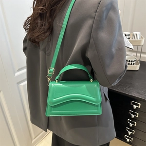 Bright green leather crossbody bag with flap and gold hardware on model in grey suit