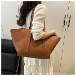 Detail of a large brown retro leather tote bag worn as an underarm shoulder bag