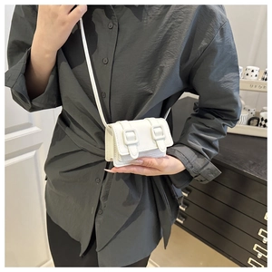 Detailed close-up of a mini white crossbody bag with double buckles shown in a lifestyle shot
