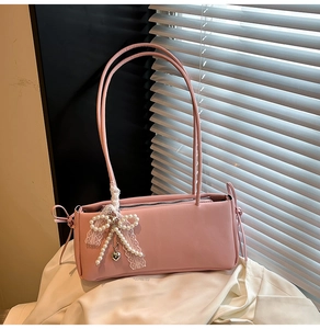 Detail of pink shoulder bag featuring side lace ribbons and a pearl heart pendant