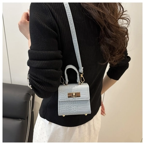 Detail of light blue mini bag with crocodile texture and gold clasp on black sweater