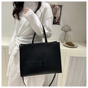 Close-up of matte black leather tote bag with embossed lettering and slim shoulder strap