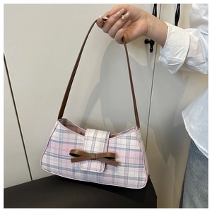 Close-up of a pink plaid underarm bag with a brown leather bow and strap detail