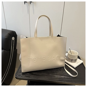 Detail of beige faux leather tote bag with large embossed lettering and detachable strap