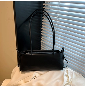 Detail of minimalist black leather shoulder bag featuring thin straps and zipper closure
