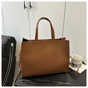 Detail showing the embossed TOTE BAG lettering on brown textured synthetic leather