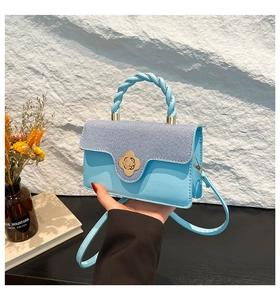 Close-up of small square bag with denim patchwork, gold flower lock, and twisted handle