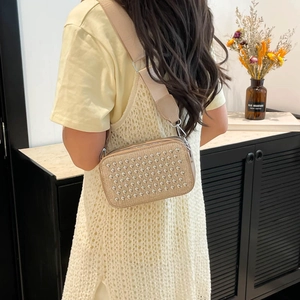 Sac à bandoulière carré à clous champagne avec large sangle porté par un mannequin femme