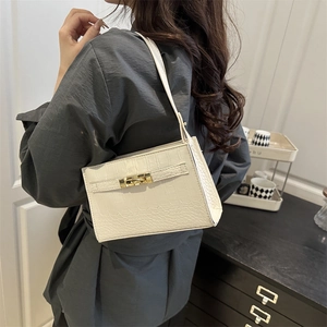 Elegant white crocodile pattern handbag with gold clasp worn by a model in interior