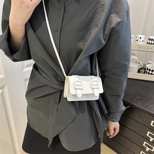 White minimalist leather crossbody bag with dual buckles shown on a female model