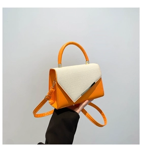Detail of orange leather and cream woven texture handbag with golden metal trim