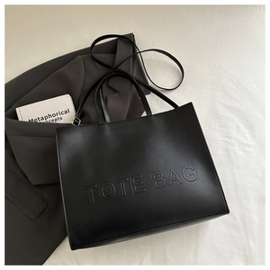 Close-up of matte black leather tote bag featuring debossed TOTE BAG lettering and texture