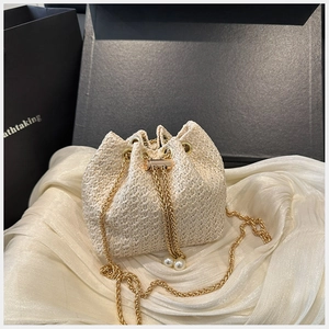 Détail du sac seau en paille beige avec bandoulière chaîne dorée et perles décoratives