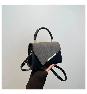 Close-up of color-block leather handbag featuring grey twill fabric and gold metal clasp