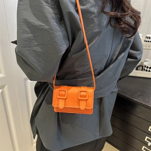 Minimalist bright orange leather crossbody bag with belt buckle detail and slim strap