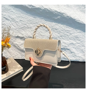 Detail of a two-tone crossbody bag with woven texture lid and flower-shaped metal lock