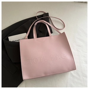 Detail of pink faux leather tote bag with debossed lettering and adjustable strap