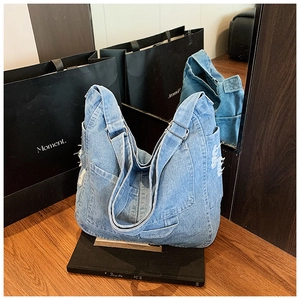 Detail view of washed blue denim shoulder bag featuring frayed edges and mirror reflection