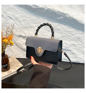 Detail of color-block crossbody bag with grey texture, black leather, and gold flower clasp