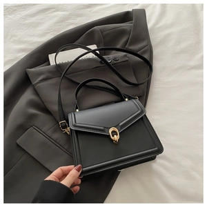 Chic black faux leather handbag with gold chain detail on a minimalist blazer backdrop