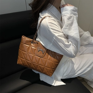 Grand sac cabas matelassé marron avec nœud argenté et bandoulière chaîne porté par un modèle