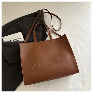 Flat lay of brown large-capacity leather tote bag with embossed lettering and shoulder strap