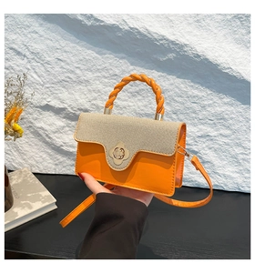 Detail of orange leather crossbody bag with woven flap and gold flower twist lock