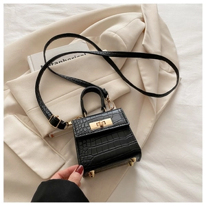 Detail of black crocodile texture mini bag with gold twist lock on a beige blazer