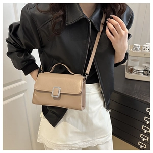 Détail d'un petit sac beige structuré avec boucle argentée porté sur une veste en cuir noir